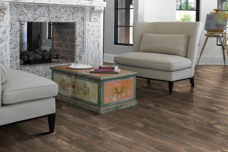 dark stained wood look tile floors in a traditional living room with a grey stone fireplace and antique coffee table